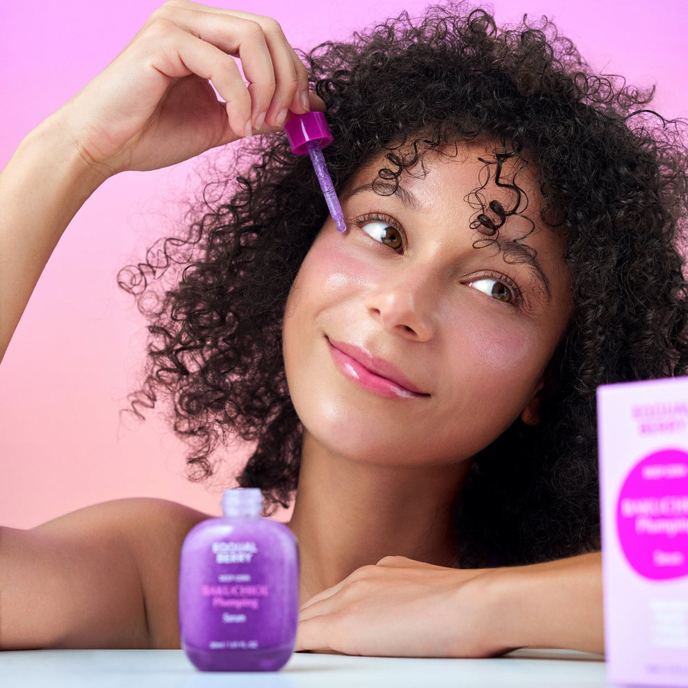 Woman applying purple hair product to her hair with a pink background