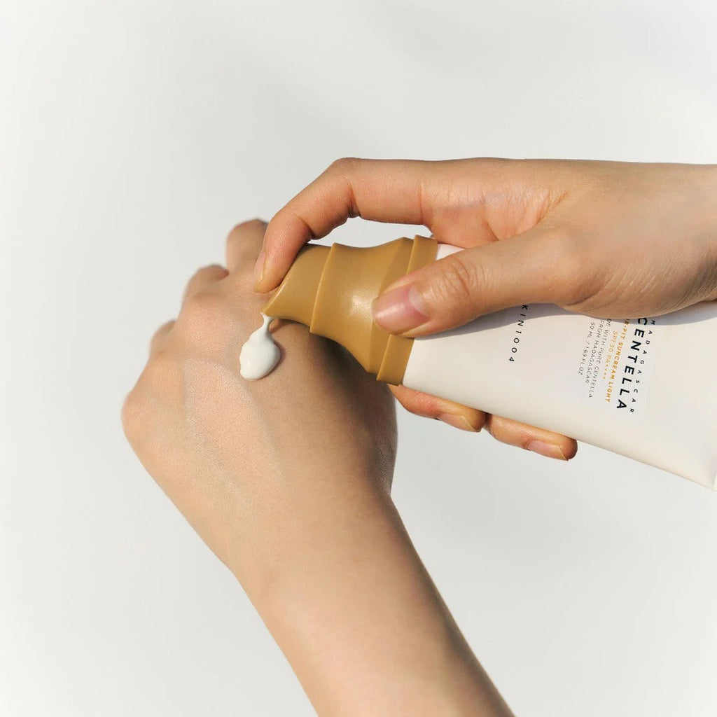 Person applying a white cream from a tube to their hand on a light gray background