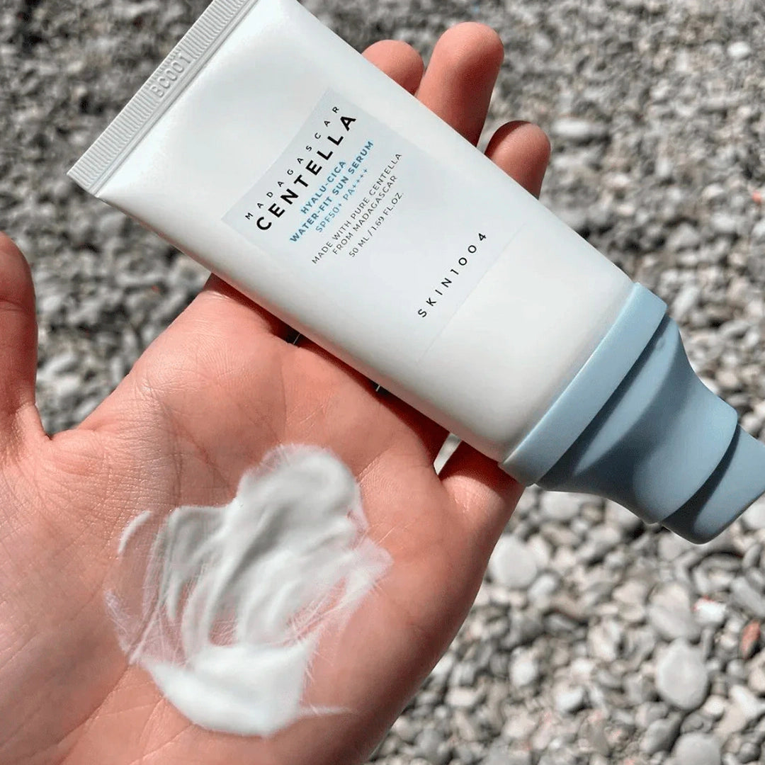 Hand holding a Skinfood Centella Cleansing Foam with foam on palm against a gravel background