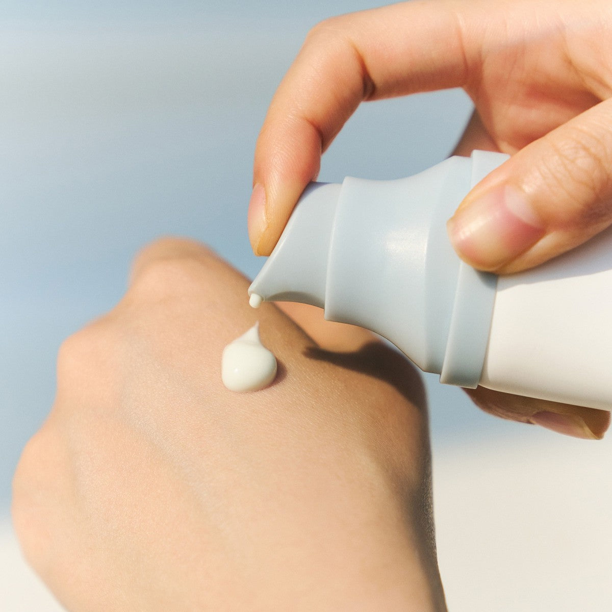 Hand applying Centella Hyalu-Cica Water-Fit Sun from a white cream against a light blue background