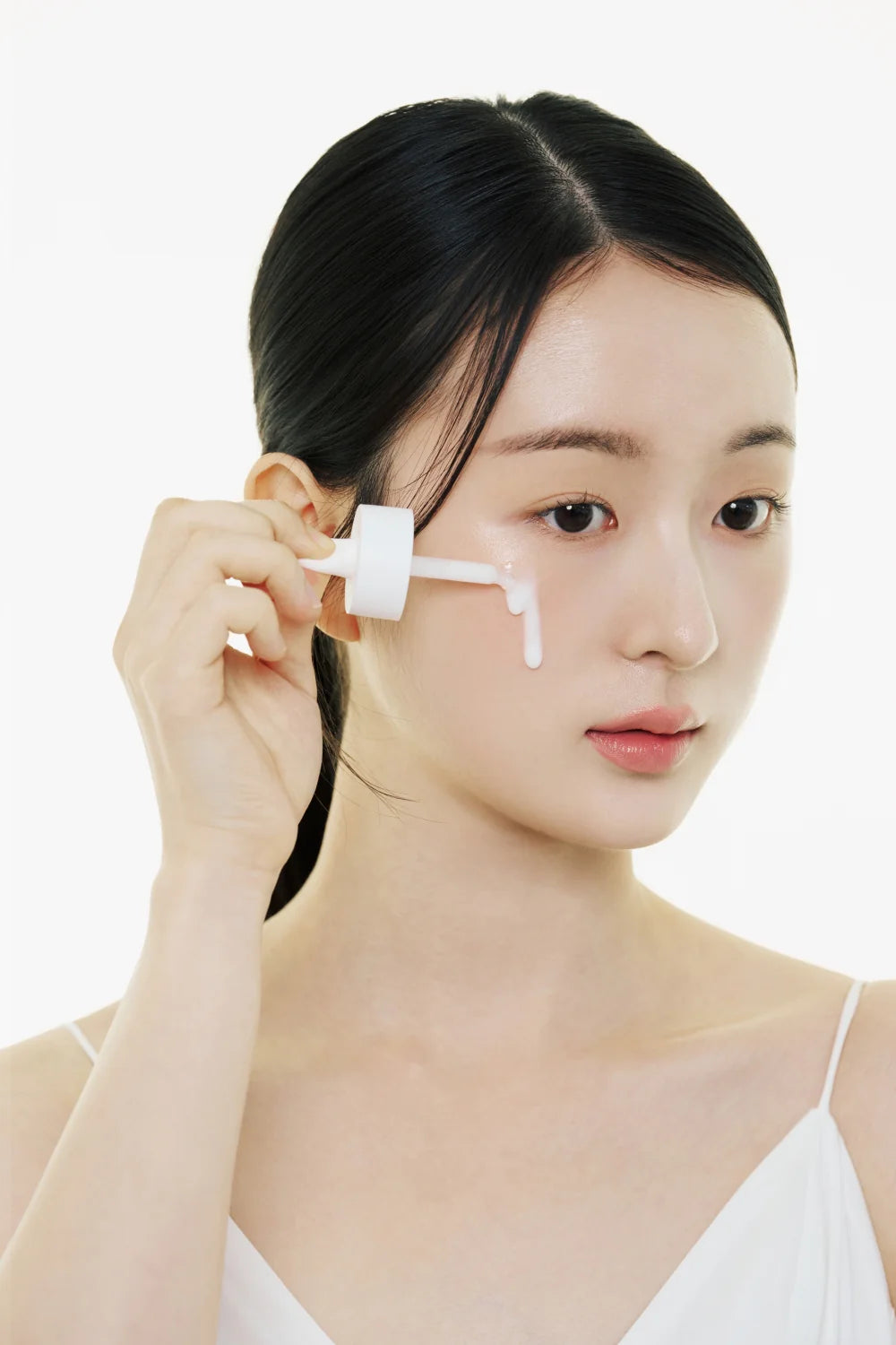 Woman applying a skincare product to her face with a white background